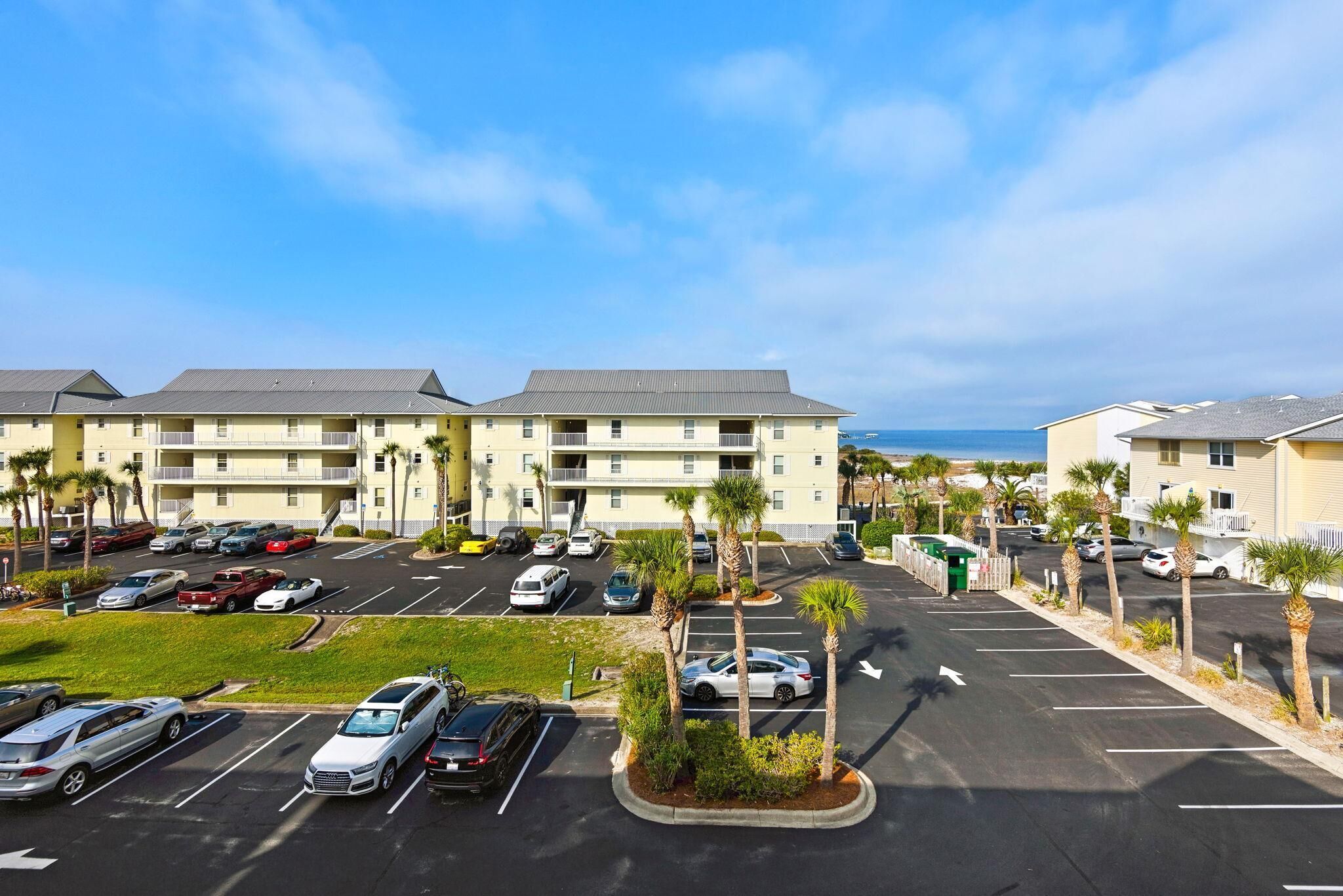 A multi-story parking garage with several cars parked, a grassy area, and a building with a flat roof in the background.