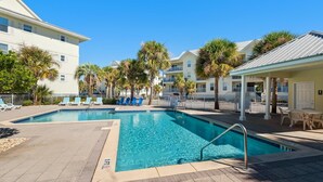 A swimming pool with lounge chairs and palm trees, surrounded by buildings with balconies. - Gulf Island 532 (Navarre)