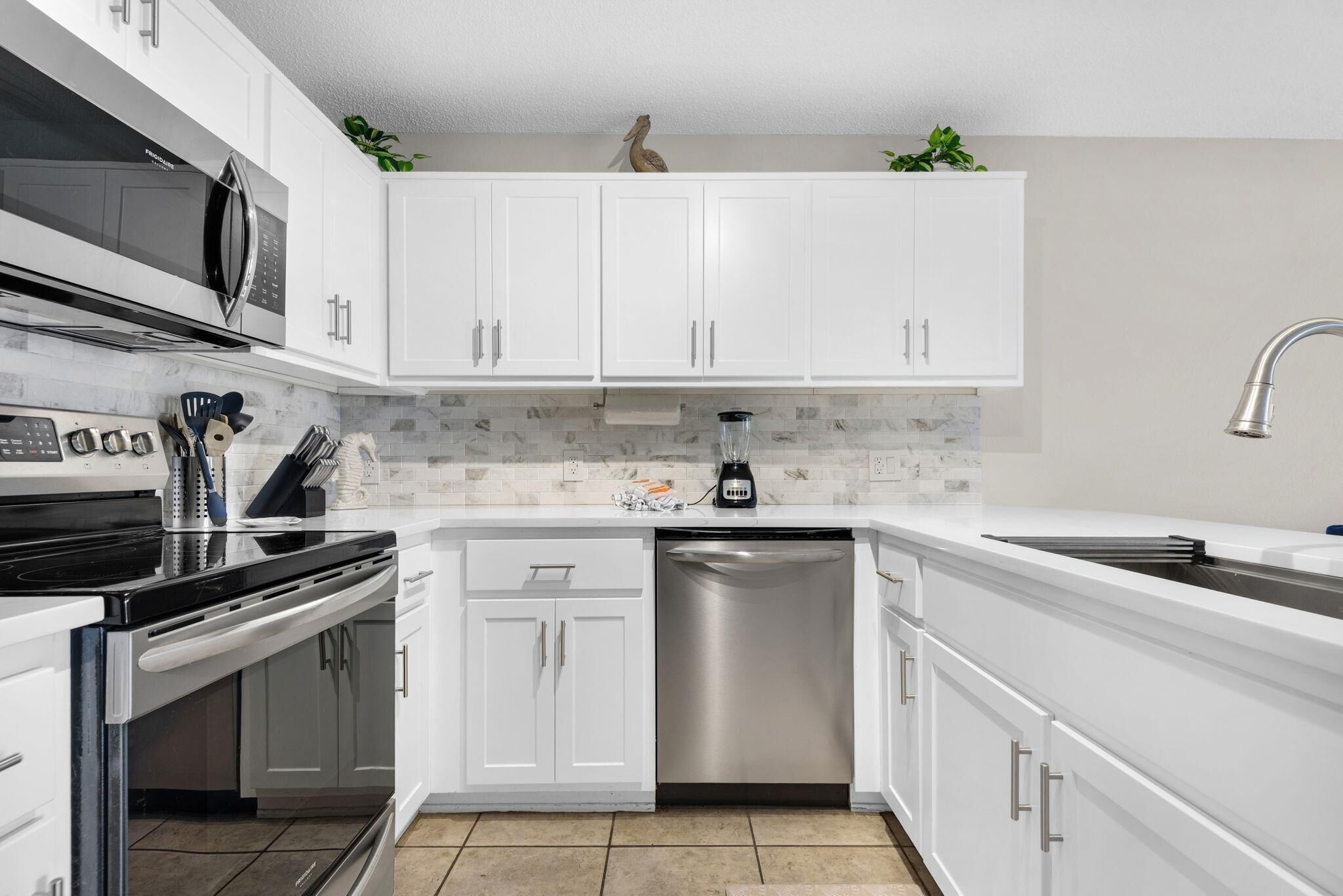 Una cocina moderna con gabinetes blancos, lavavajillas de acero inoxidable, microondas y fregadero.