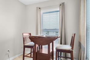 A dining area with a wooden table and two chairs, a window with blinds, and a power outlet on the wall. - Gulf Island 532 (Navarre)