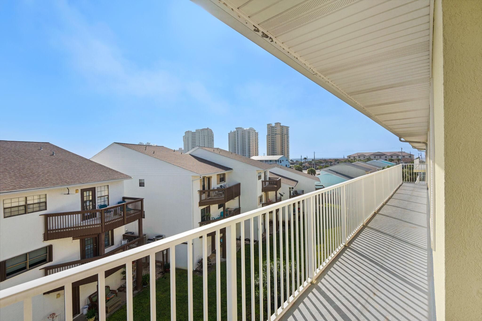 A residential building with multiple balconies, a covered walkway, and a view of taller buildings in the distance.