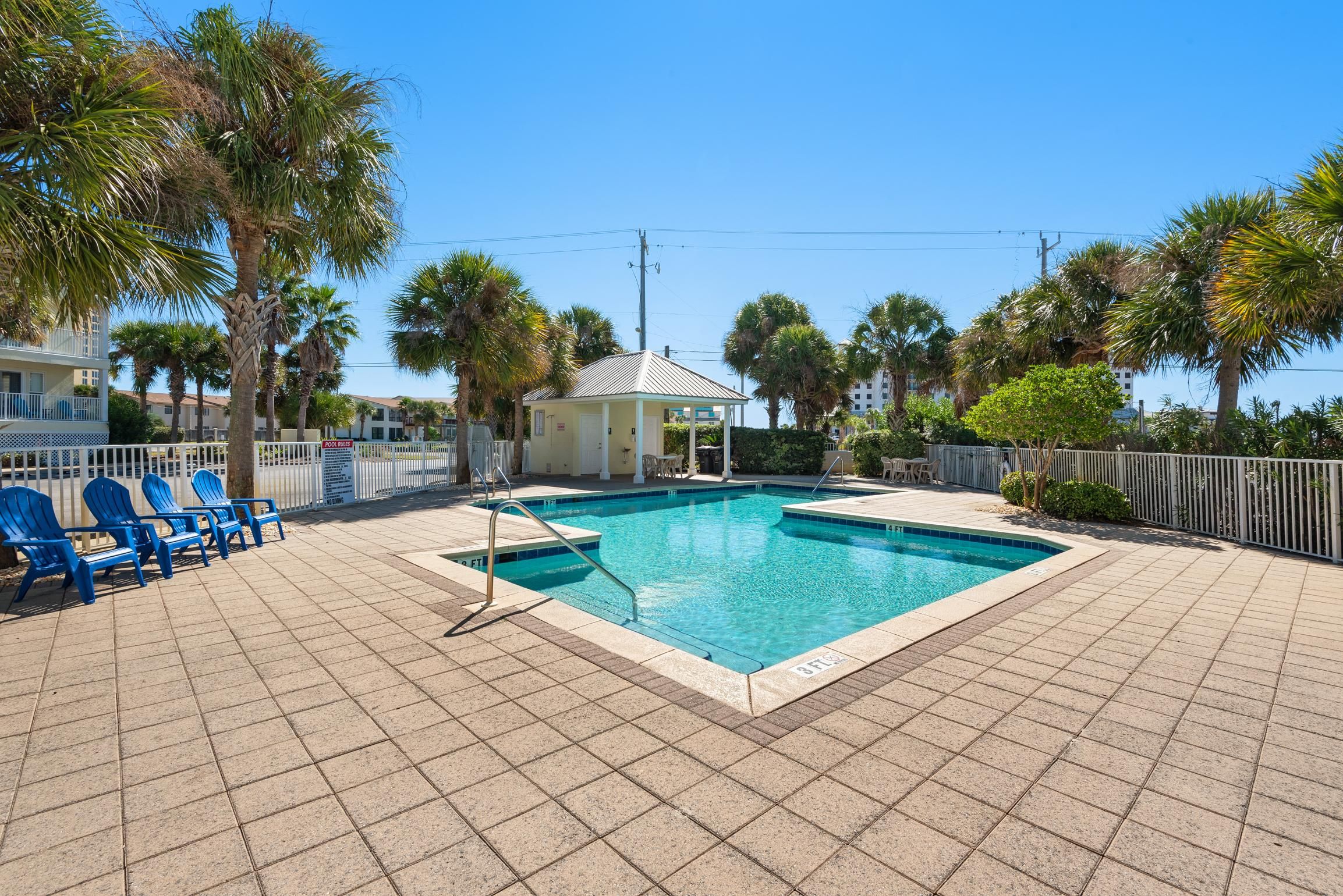 A swimming pool with blue chairs, surrounded by palm trees and a small gazebo.