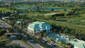 Um campo de golfe com um edifício grande e telhado verde, rodeado por palmeiras e corpos de água.