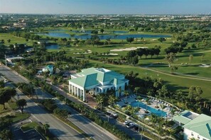 A golf course with a large building featuring a green roof, surrounded by palm trees and water bodies. - Amazing 1BR Apt w/ Private Balcony + Amenities (Doral)