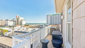 Een balkon met buitenmeubilair, uitzicht op het strand en een hoog gebouw op de achtergrond.