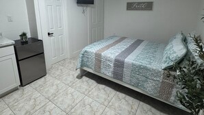 Quarto com cama, televisão fixada na parede, frigorífico e planta em vaso.
