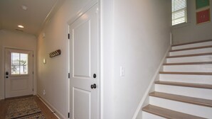 Un pasillo con un tapete estampado, una puerta blanca y una escalera de madera.