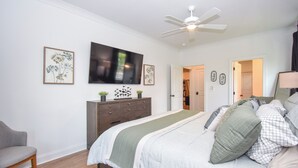 Un dormitorio con cama, televisión, ventilador de techo, cómoda y silla.