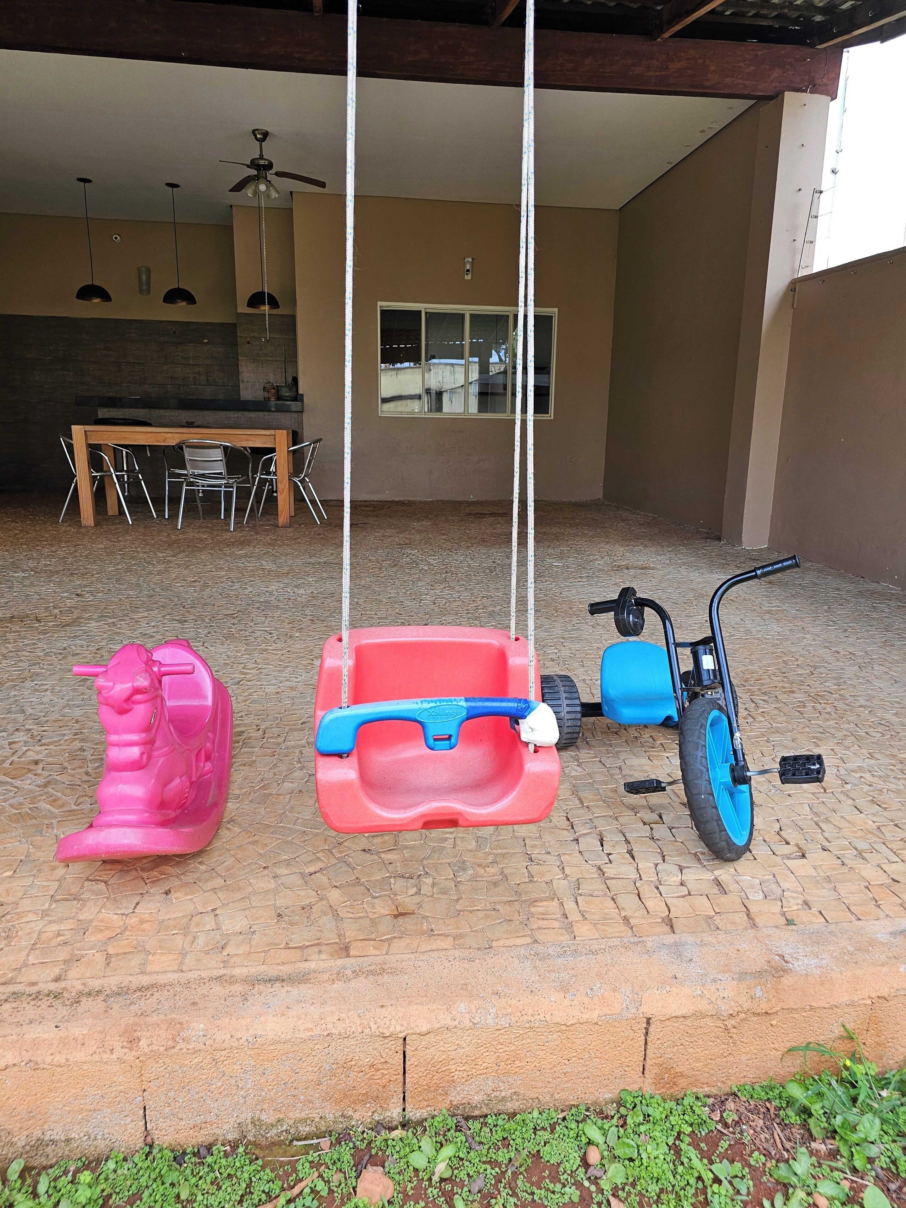 A patio with a swing set, a scooter, and a dining area with a table and chairs.