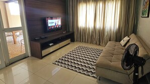 A living room with a flat-screen TV, a sofa, a fan, and a patterned rug.