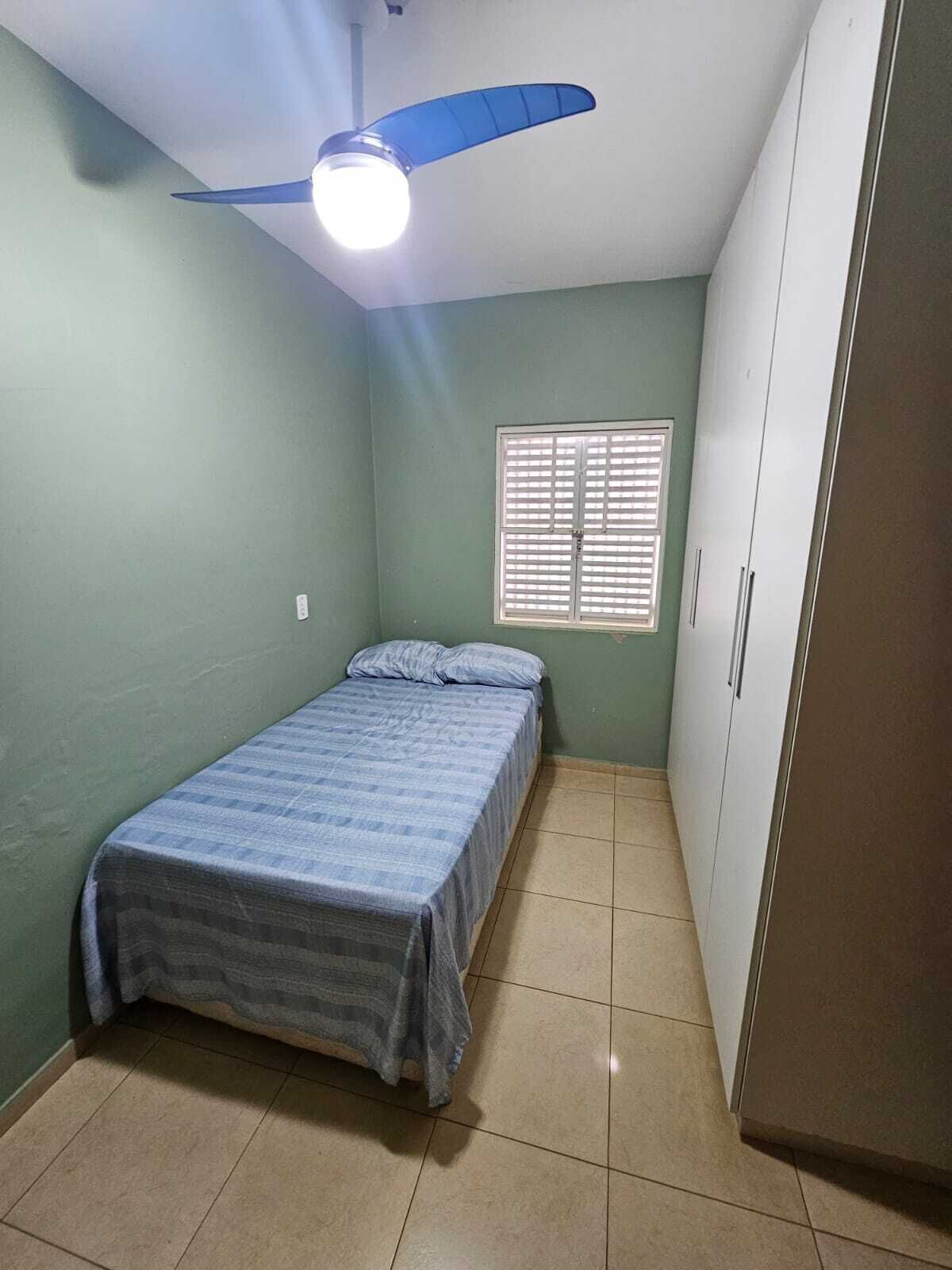 Um quarto com cama, ventoinha no teto, janela com persianas e guarda-roupa.