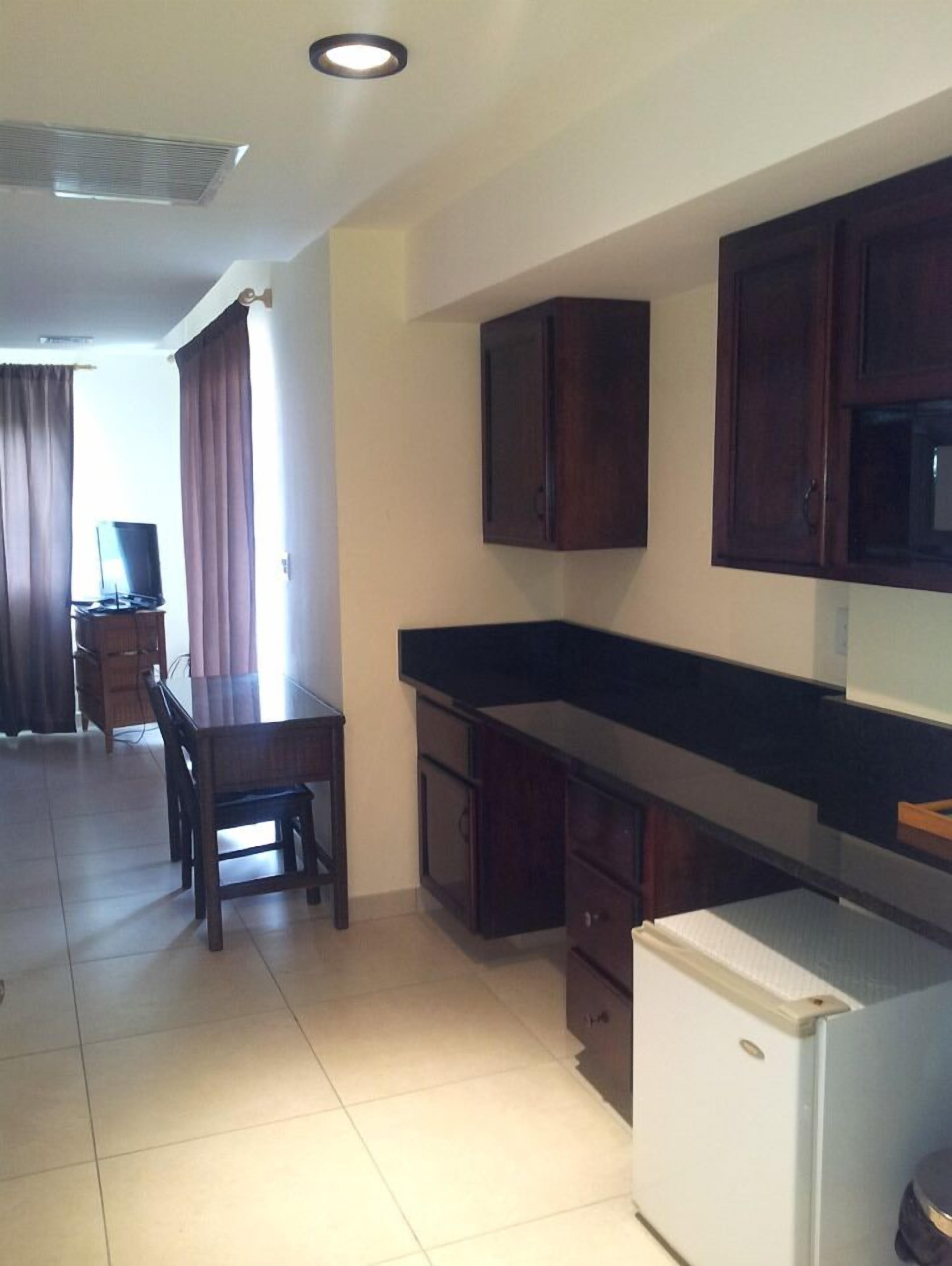 A compact kitchen with a refrigerator, a dining table with chairs, wooden cabinets, and a television.