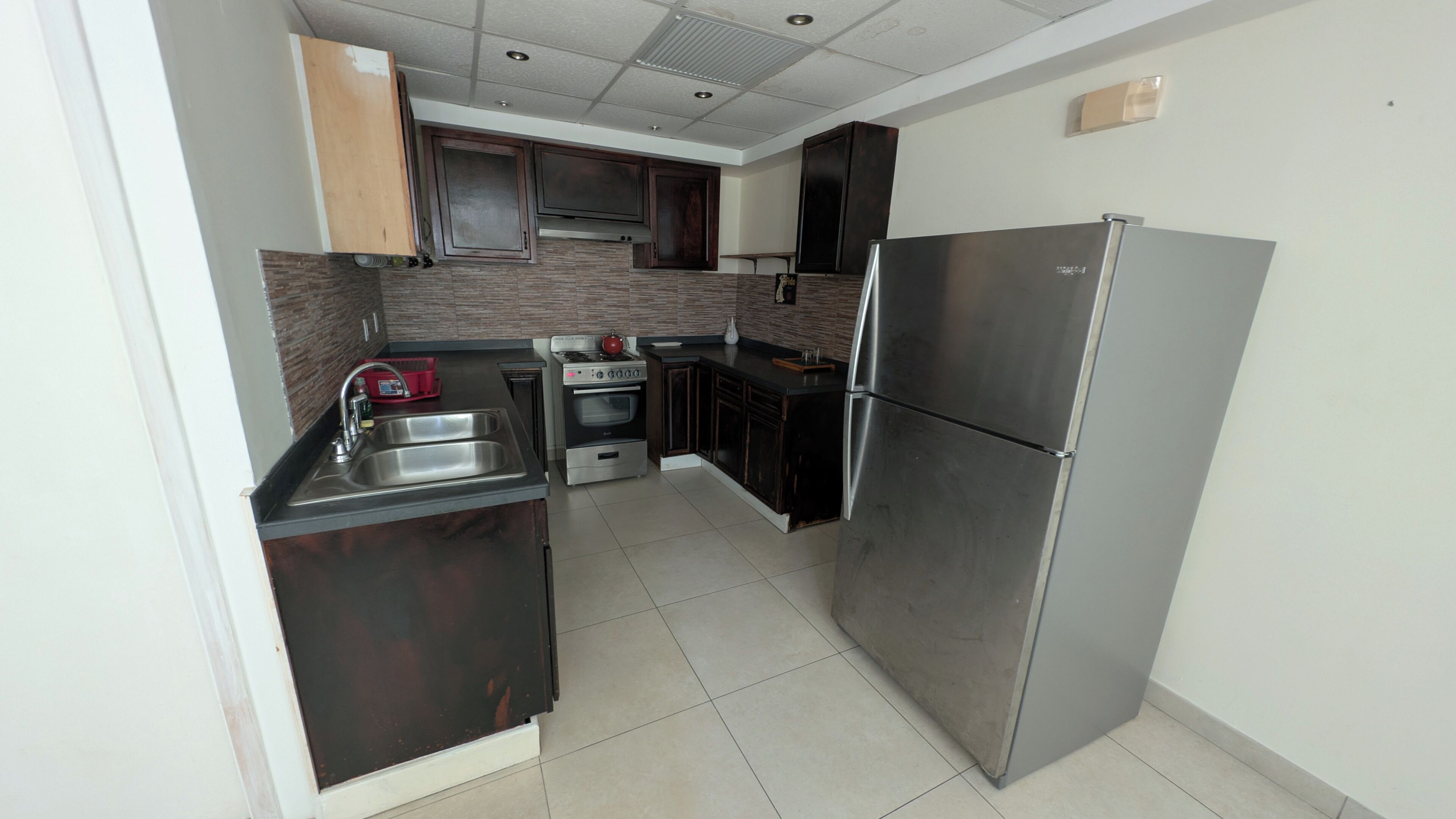 A modern kitchen with dark cabinetry, stainless steel appliances, and a tiled floor.