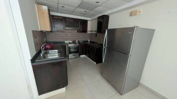 A modern kitchen with dark cabinetry, stainless steel appliances, and a tiled floor.