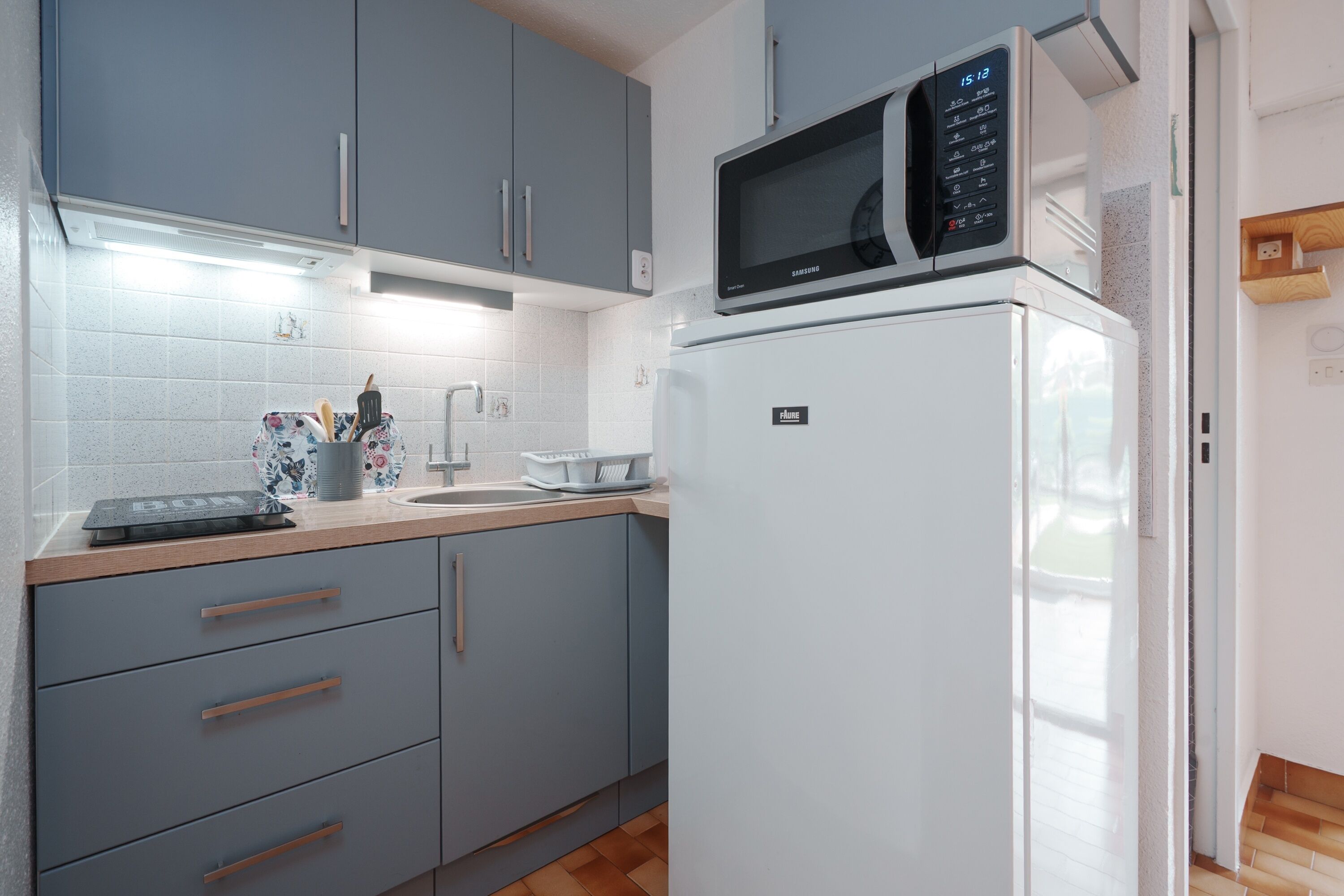 Una cocina con gabinetes grises, un refrigerador blanco, un microondas y una encimera de madera.