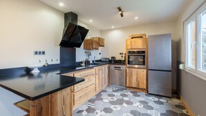 A modern kitchen with wooden cabinets, a black countertop, a stainless steel refrigerator, and a hexagonal patterned floor. - Châlet Pré Gaillard - proche du centre la Bresse (La Bresse)