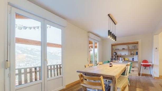 A dining area with a wooden table and chairs, a bookshelf, and a view through large windows. - Châlet Pré Gaillard - proche du centre la Bresse (La Bresse)