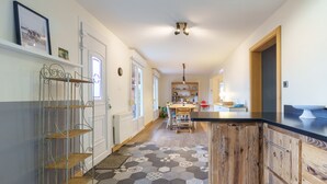 A kitchen with a central island, a dining area with chairs, and a hallway with a patterned floor. - Châlet Pré Gaillard - proche du centre la Bresse (La Bresse)