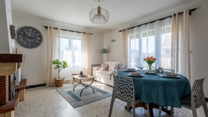 A dining area with a table set for four, a clock on the wall, and a sofa in the background. - La Petite Solognote - Proche Châteaux de la Loire (Cour-Cheverny)