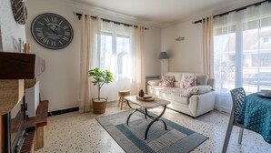 A living room with a sofa, a coffee table, a clock, and a window with curtains. - La Petite Solognote - Proche Châteaux de la Loire (Cour-Cheverny)
