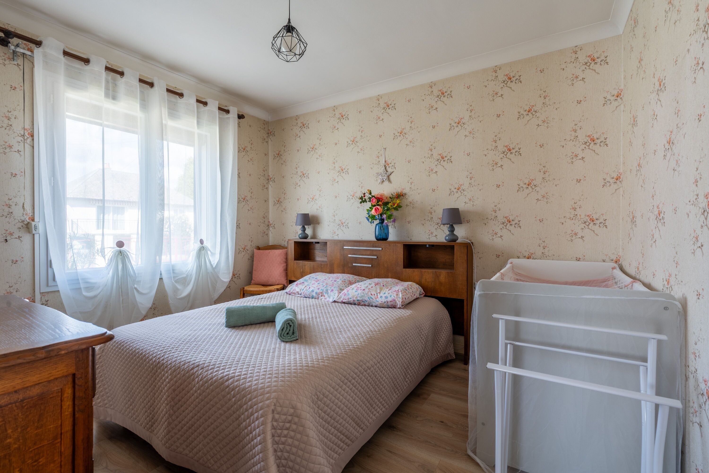 A bedroom with a bed, bedside tables, a dresser, a radiator, and a window with curtains.