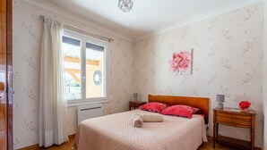 A bedroom with a bed, a nightstand, a window with curtains, a wall clock, and a floral wallpaper. - La Petite Solognote - Proche Châteaux de la Loire (Cour-Cheverny)