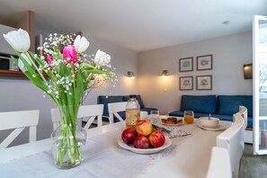 Ein Esstisch mit Blumen in einer Vase, einer Obstschale, einer Flasche und einem Glas.