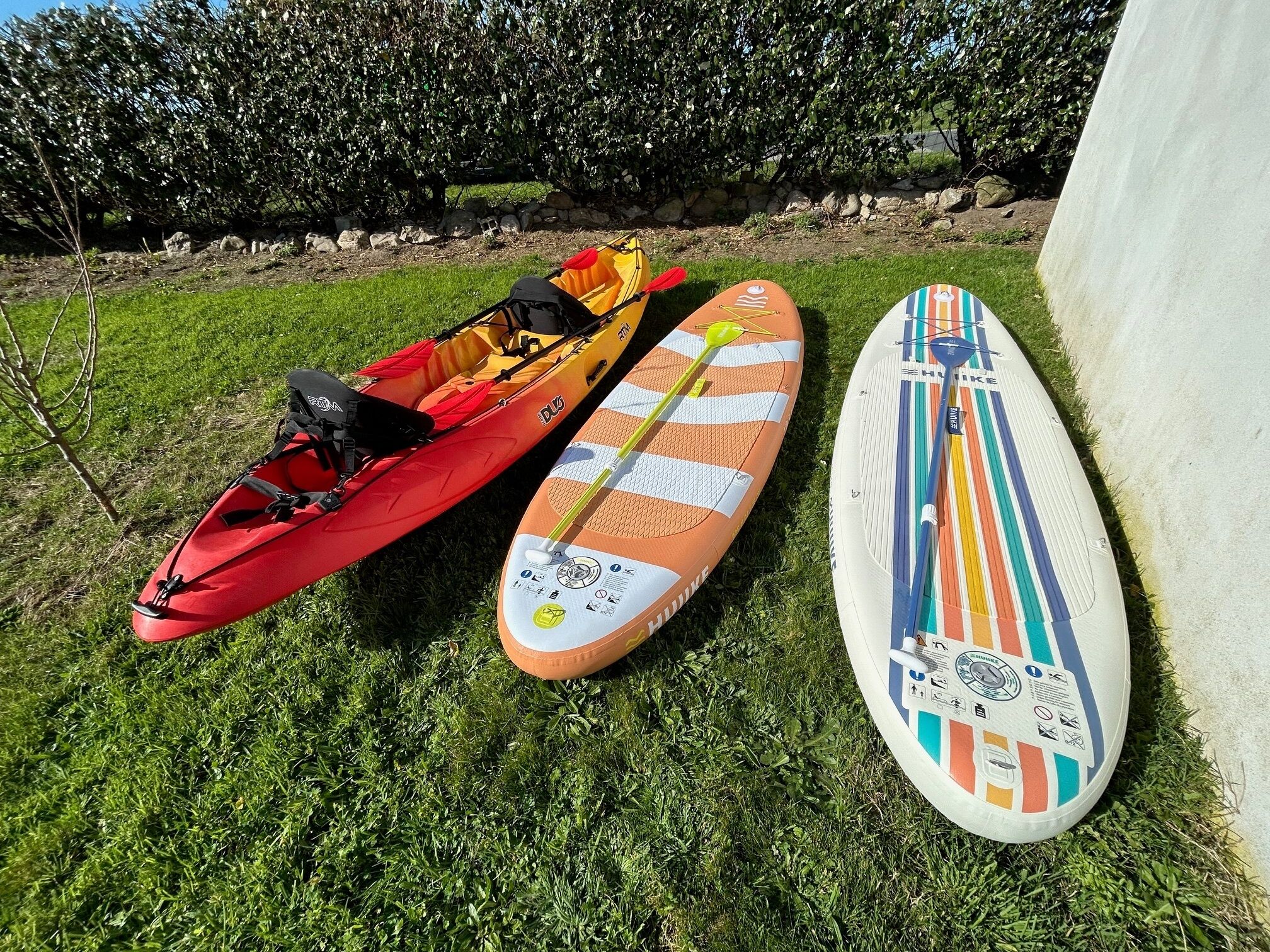 A red kayak and two paddleboards on grass.