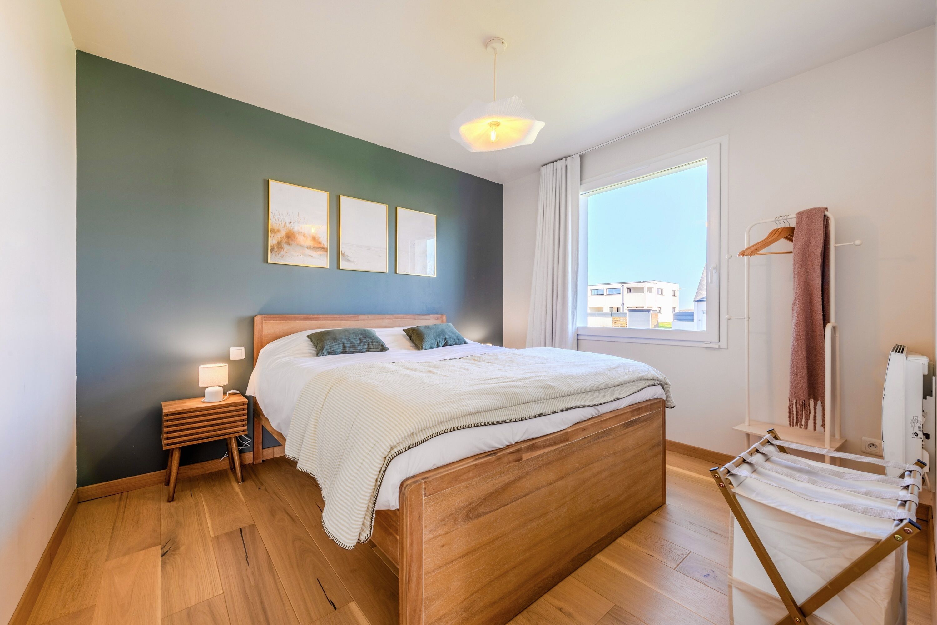 Un dormitorio con una cama de madera, mesitas de noche, una lámpara colgante, una ventana con vistas y un perchero para toallas.