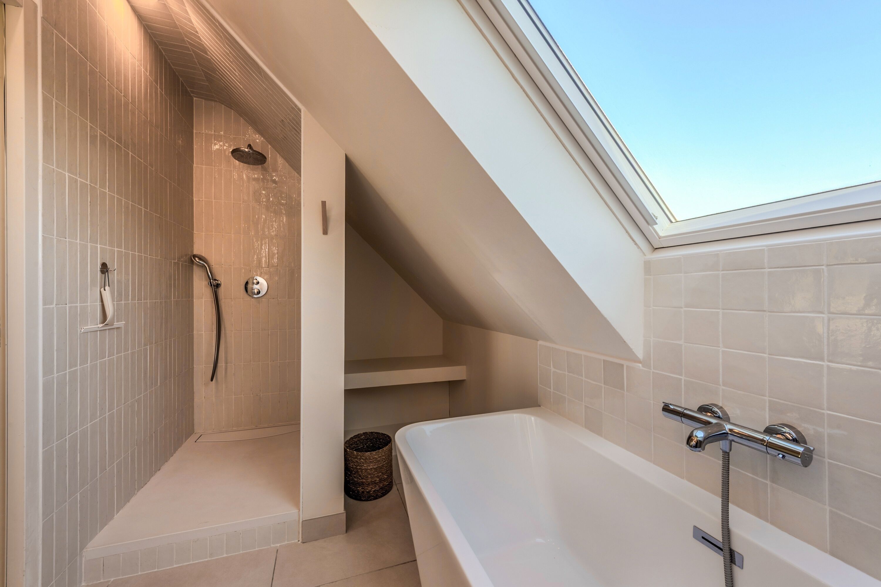 Ein modernes Badezimmer mit Dachfenster, einer begehbaren Dusche und einer freistehenden Badewanne.