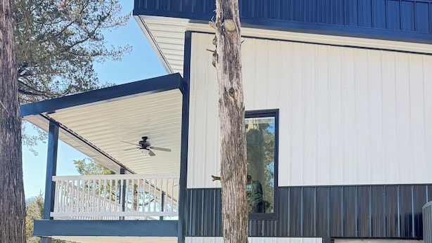 Un edificio moderno de dos pisos con un balcón, un árbol y un camino de grava.