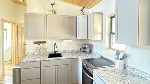 Una cocina moderna con vigas de madera en el techo, encimeras de granito y muebles de cocina blancos.