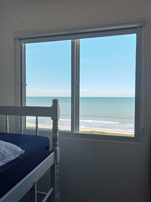 Una habitación con una cama, un ventanal con vista a la playa y una puerta.