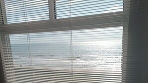 Ein Zimmer mit Bett, Fenster mit Jalousien und Blick auf den Strand.