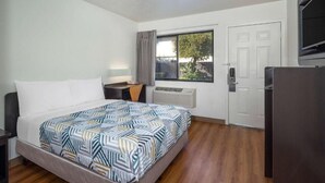 A hotel room with a bed, a desk, a TV, a window, and a door. - Vagabond Inn - Santa Barbara (Santa Barbara)