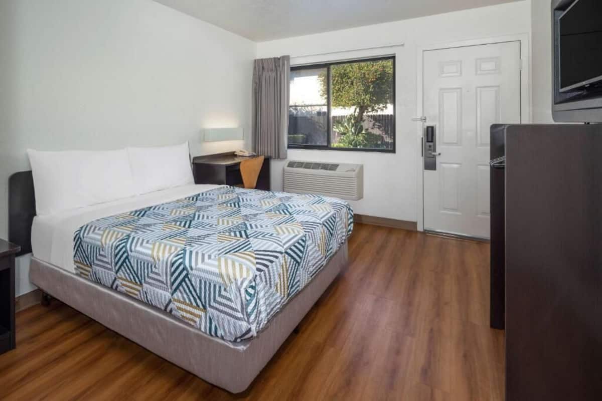 A hotel room with a bed, a desk, a TV, a window, and a door.