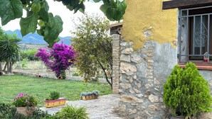 Un muro de piedra, un edificio amarillo y un jardín con diversas plantas.