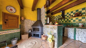 Una cocina rústica con chimenea de piedra, vigas de madera y salpicadero a cuadros.
