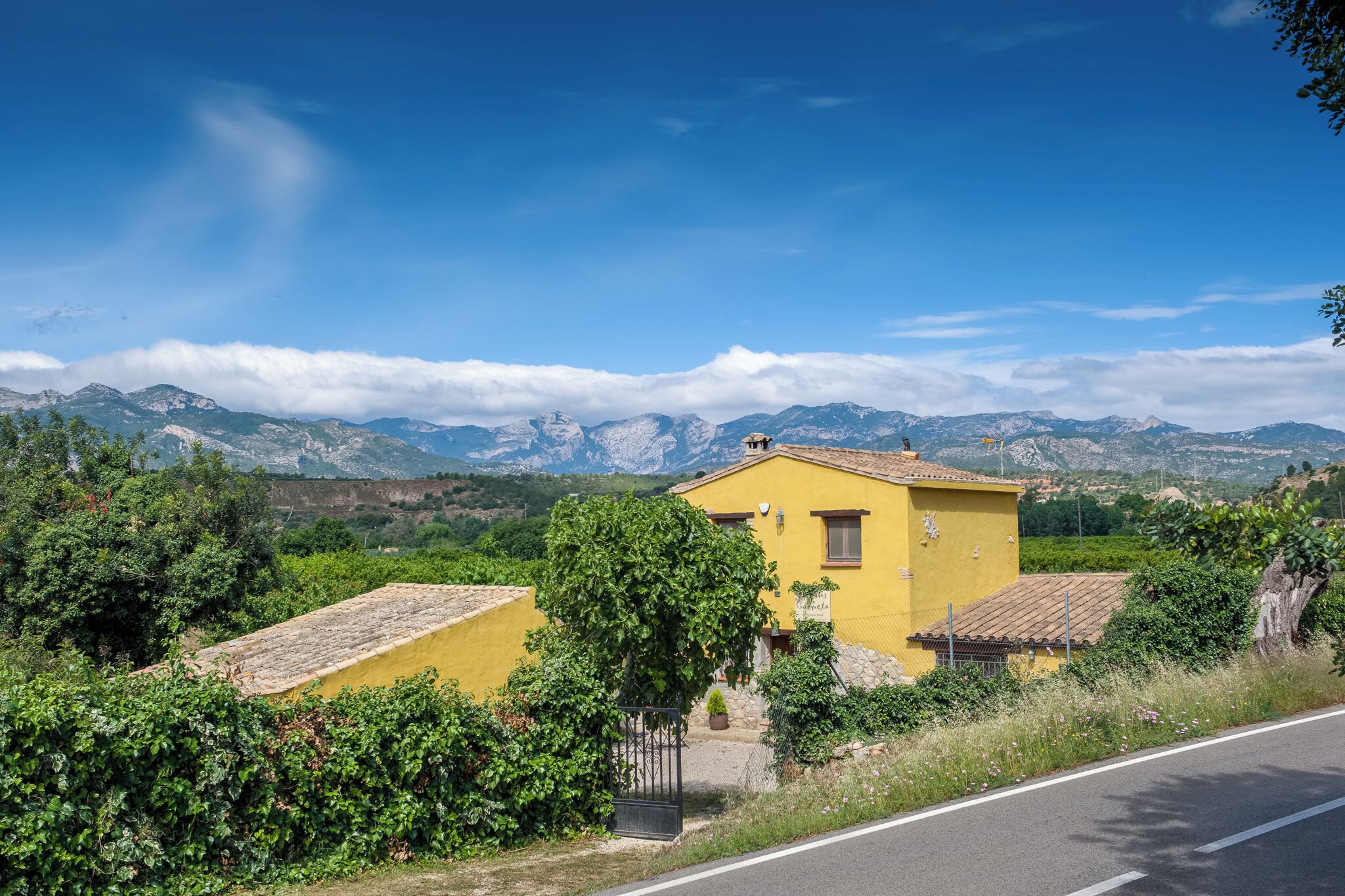 A yellow building with a tiled roof, surrounded by greenery and mountains in the background.