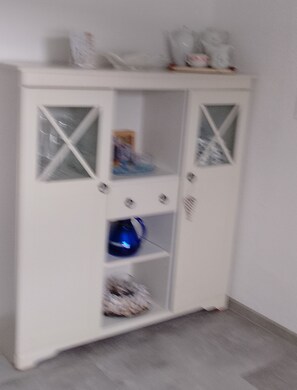 A white cabinet with glass doors, shelves, and a blue object on the bottom shelf. - Beautiful Apartment in the Rhön (Kaltennordheim)
