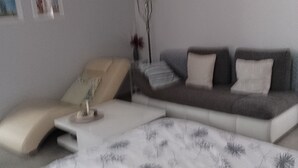 En moderne stue med sofa, et lille bord og en seng med blomstret dyne.