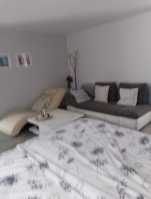 A modern living room with a sofa, a small table, and a bed with a floral bedspread. - Beautiful Apartment in the Rhön (Kaltennordheim)