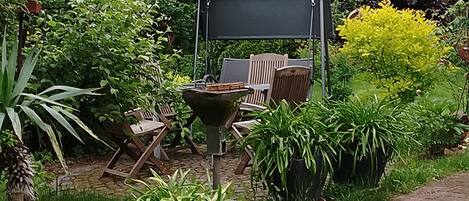Un patio jardín con una mesa y sillas, un conjunto de columpios y diversas plantas en macetas.
