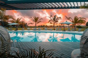 A swimming pool with lounge chairs and umbrellas, surrounded by palm trees and a sunset view. - Cozy 1-bedroom apartment with AC in Punta Cana (Punta Cana)