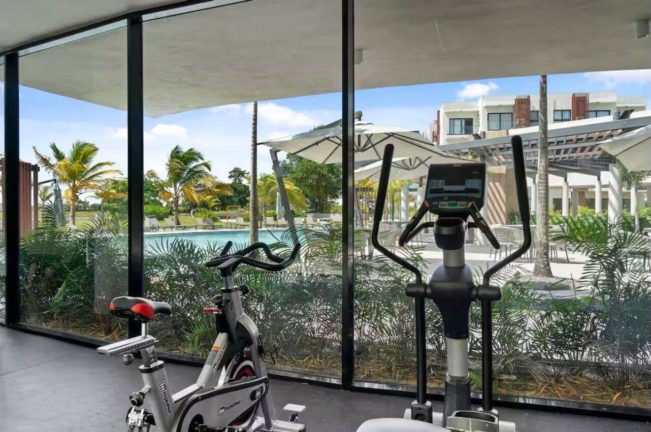 Una cyclette e un tapis roulant in una stanza con ampie finestre che danno su una piscina e palme.