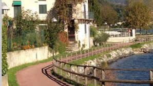 Un edificio con un sentiero lastricato che conduce a un corpo d'acqua, circondato da vegetazione e montagne sullo sfondo.