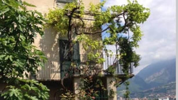 Un edificio con un balcone, una zona verde e vista su un lago e montagne.