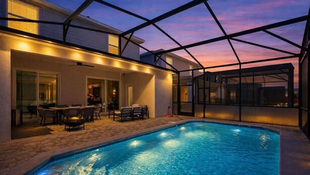 Une piscine entourée de parois en verre, un patio avec des sièges et une vue imprenable sur le coucher de soleil.