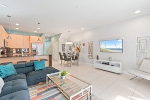 Ein modernes Wohnzimmer mit Sofa, Couchtisch, Fernseher und einem Essbereich mit Stühlen und Tisch.