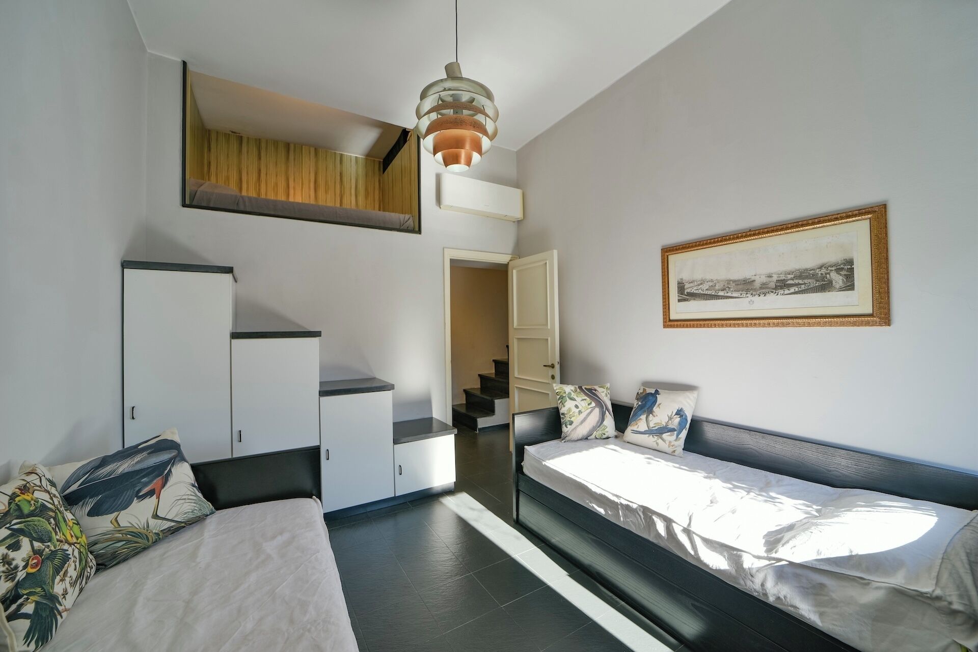 Habitación de hotel pequeña con cama, sofá, armario, escalera y un cuadro en la pared.